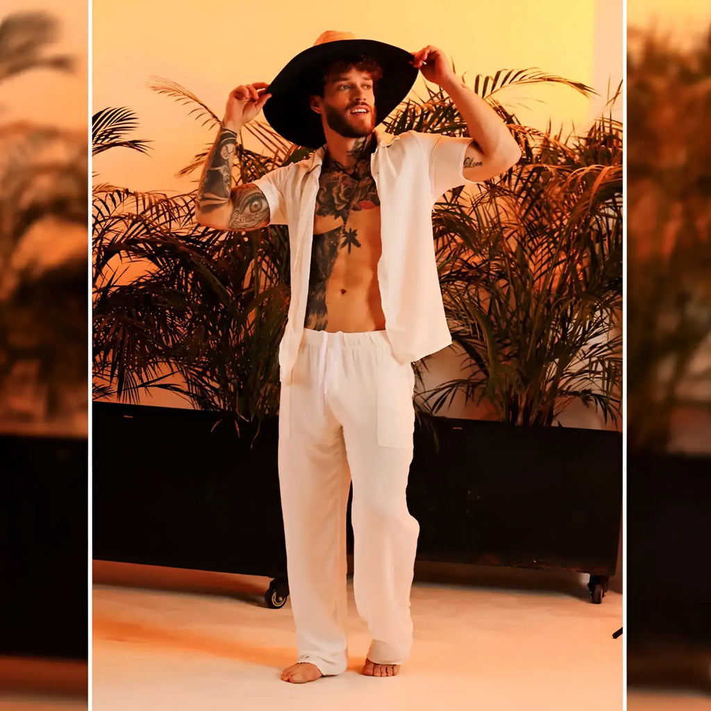 A man wearing gigo chalis beige loose-fitting pants paired with a wide-brimmed black hat and an open white shirt