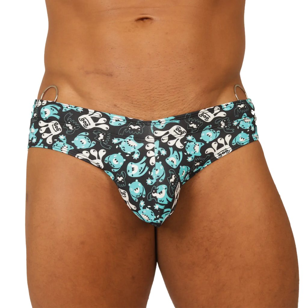 Black gigo comics swimbrief swim trunks with teal and white cartoon creatures and metal rings at the waistband
