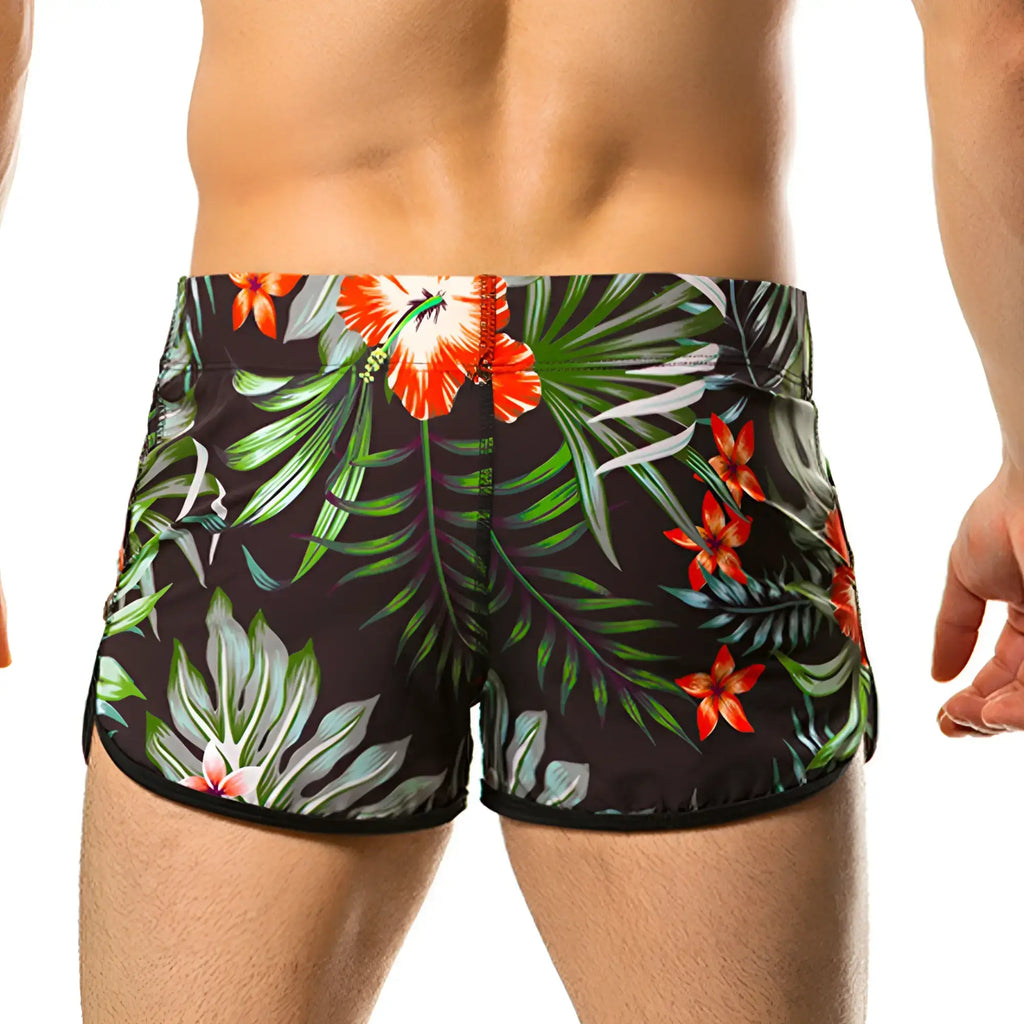 Black swim trunks from Gigo Garden Beachwear with vibrant orange hibiscus flowers and green palm leaves tropical print