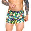 Vibrant yellow gigo macaws swim trunks with tropical blue green red and purple leaf and flower pattern for beachwear