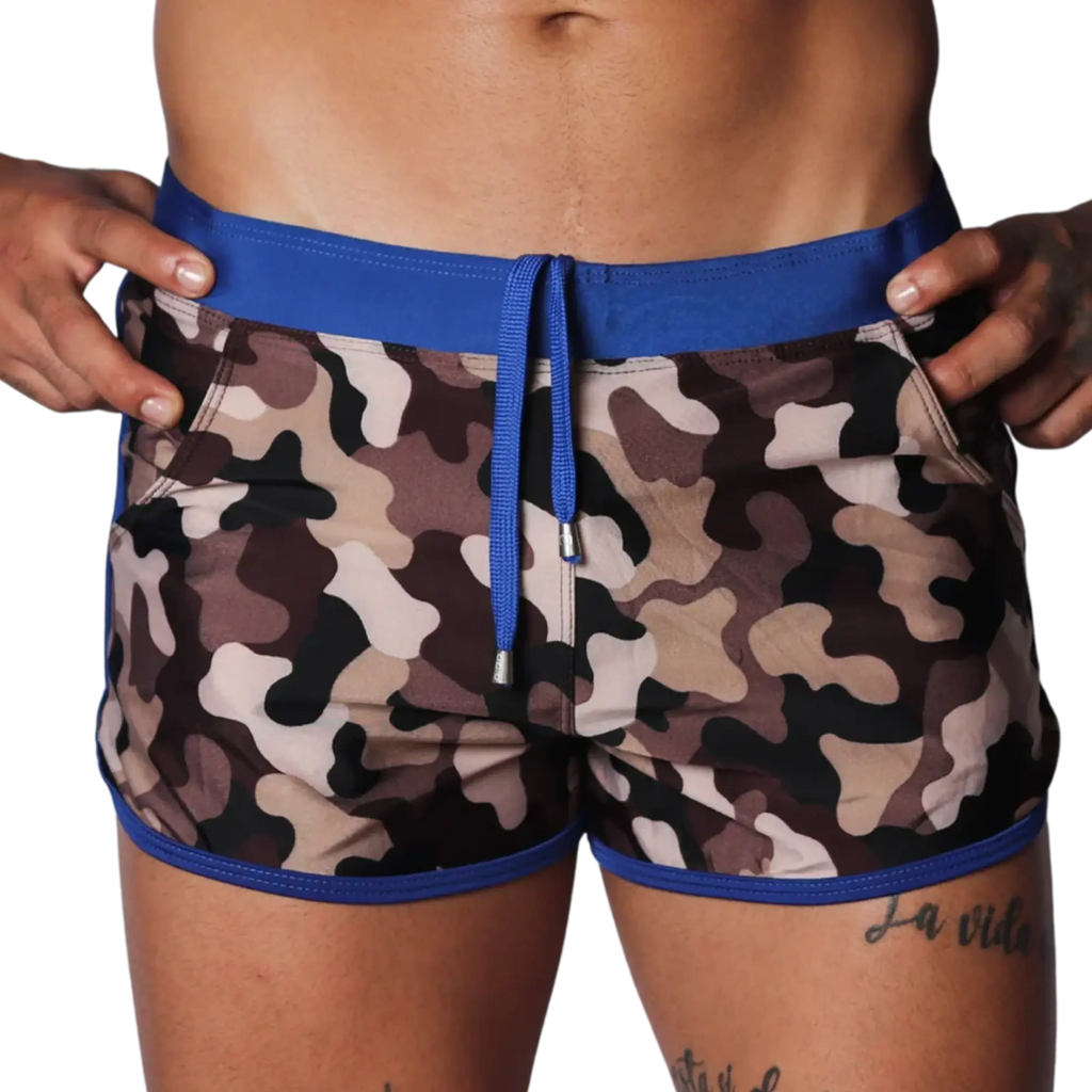 Camo print swim shorts with a blue elastic waistband, matching drawstring, and blue trim detail on a black background.