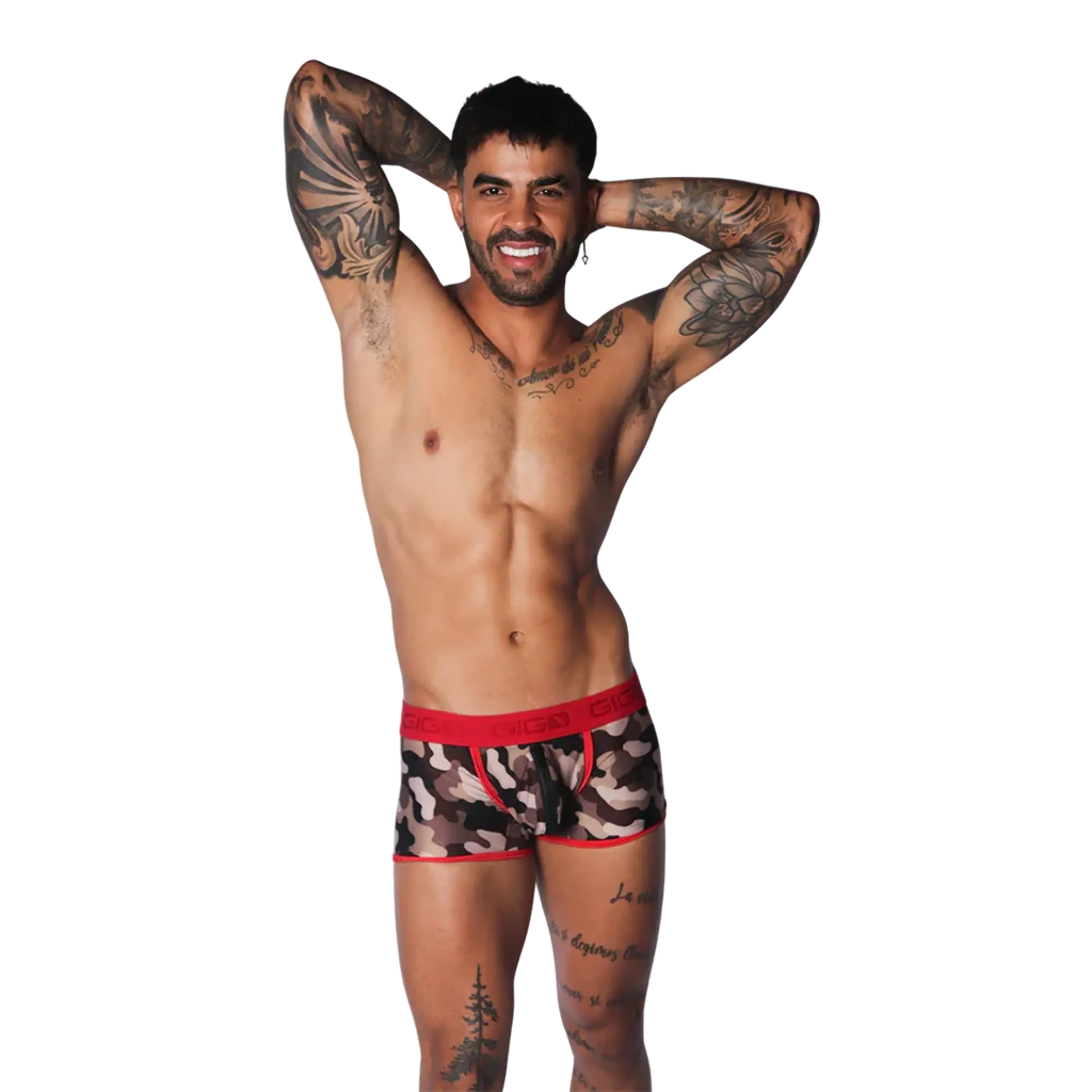 Camouflage print trunk with red trim and branded elastic waistband, worn by a tattooed model on a black background.