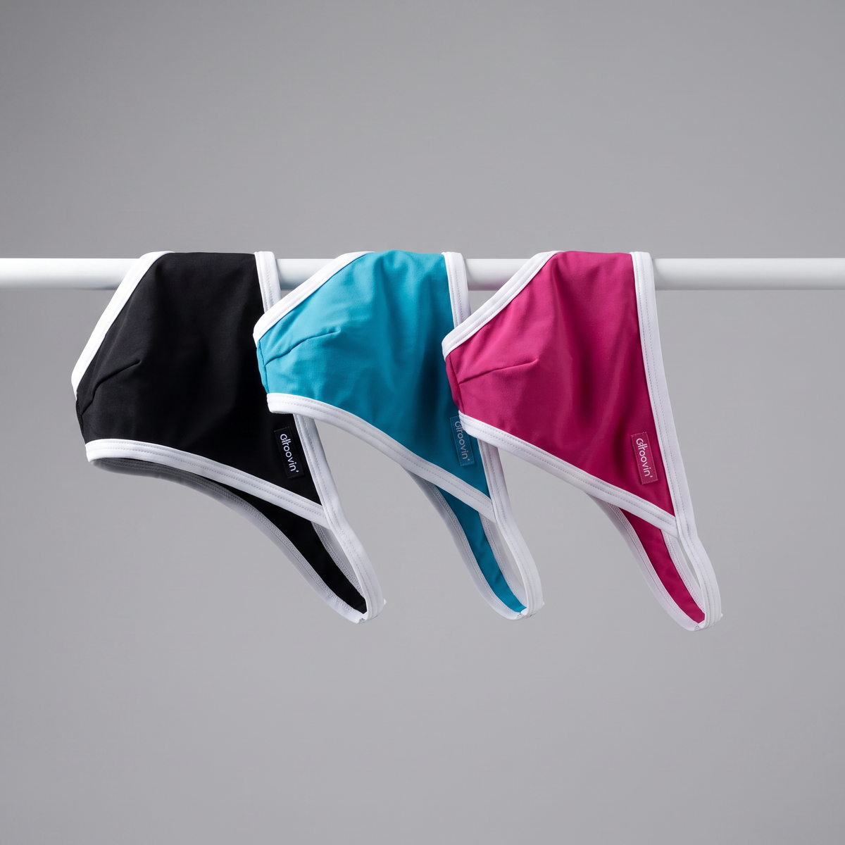 Three Groovin' accent string bikinis in black, blue, and pink with white trim, draped on a rail.