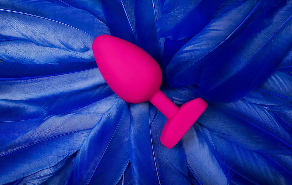 A vibrant pink silicone gvibe gplug large bioskin sweet raspberry butt plug resting on deep blue feathers