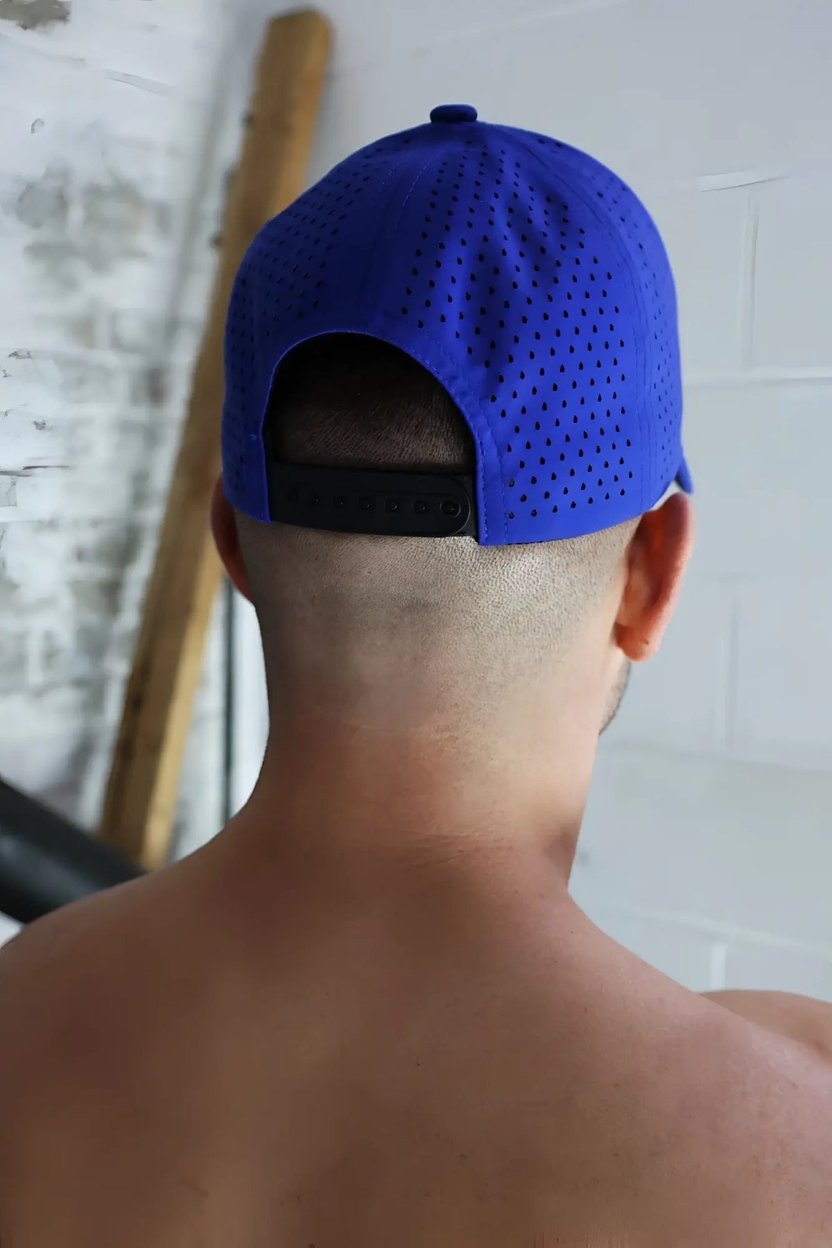 A vibrant royal blue perforated baseball cap with a black adjustable strap shown from the back from Gymnetixxx Hat