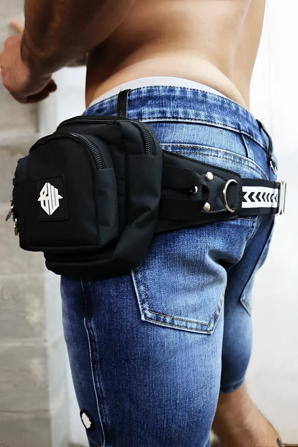Black hustler waist pack with white geometric logo patch and silver metal hardware in tactical style design