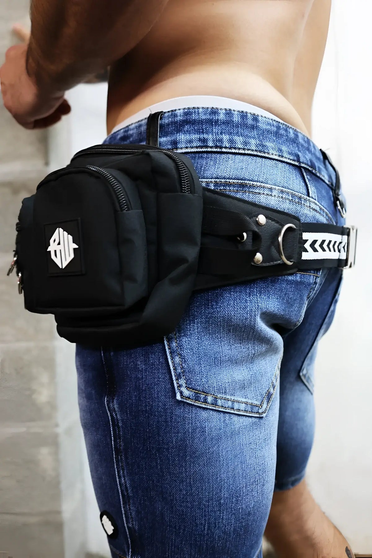 Black hustler waist pack with white geometric logo patch and silver metal hardware in tactical style design