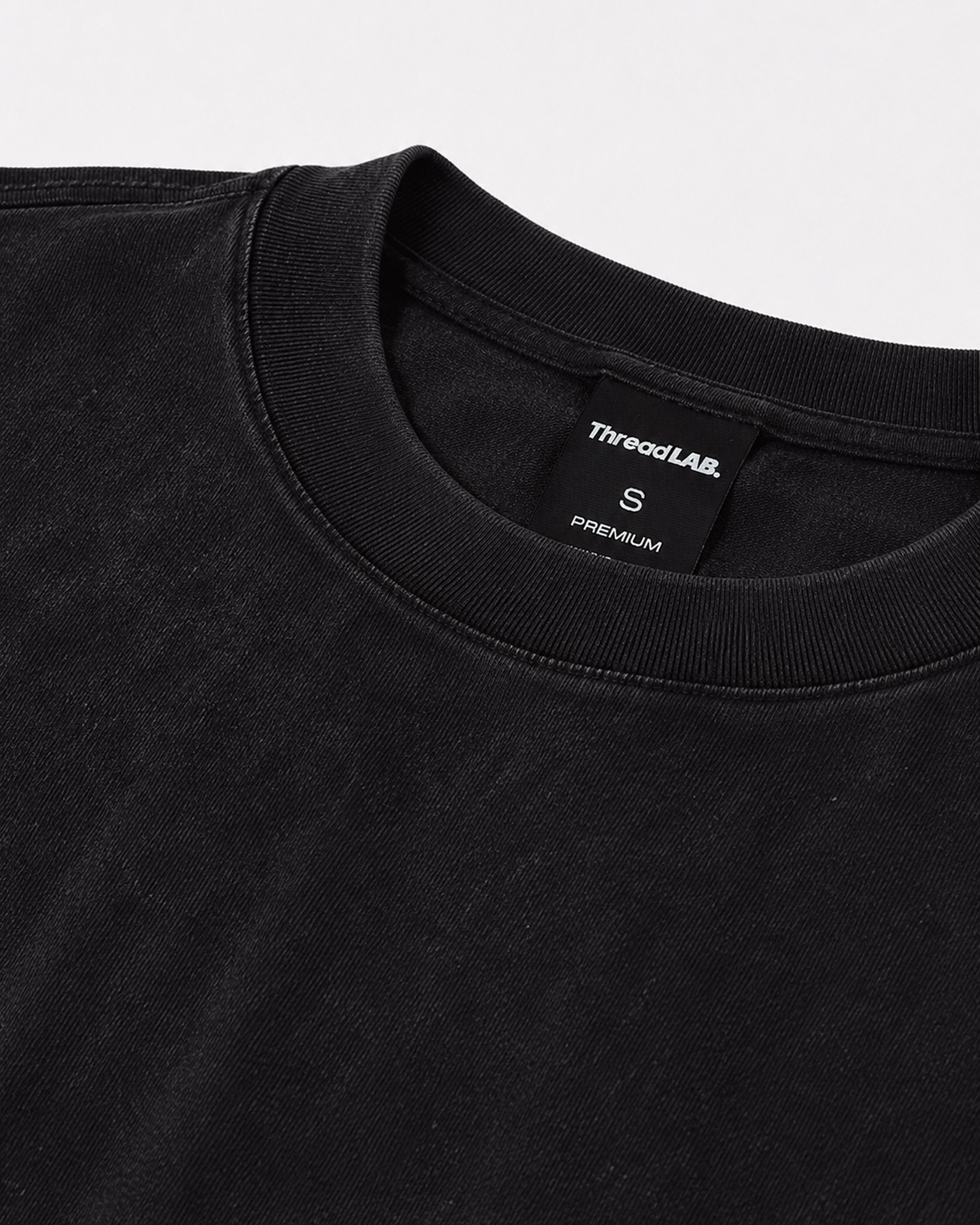 Close-up of a black crew-neck premium t-shirt with a ribbed collar and ThreadLAB size small tag.