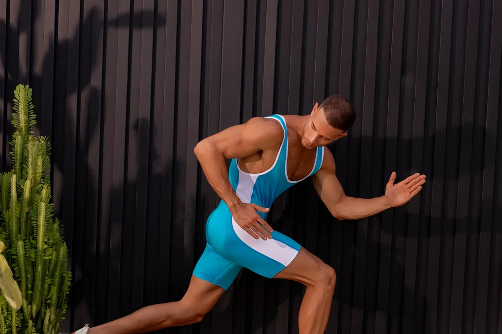 A muscular man wearing a turquoise jor 2216 fighter bodysuit in sleek seamless athletic singlet material