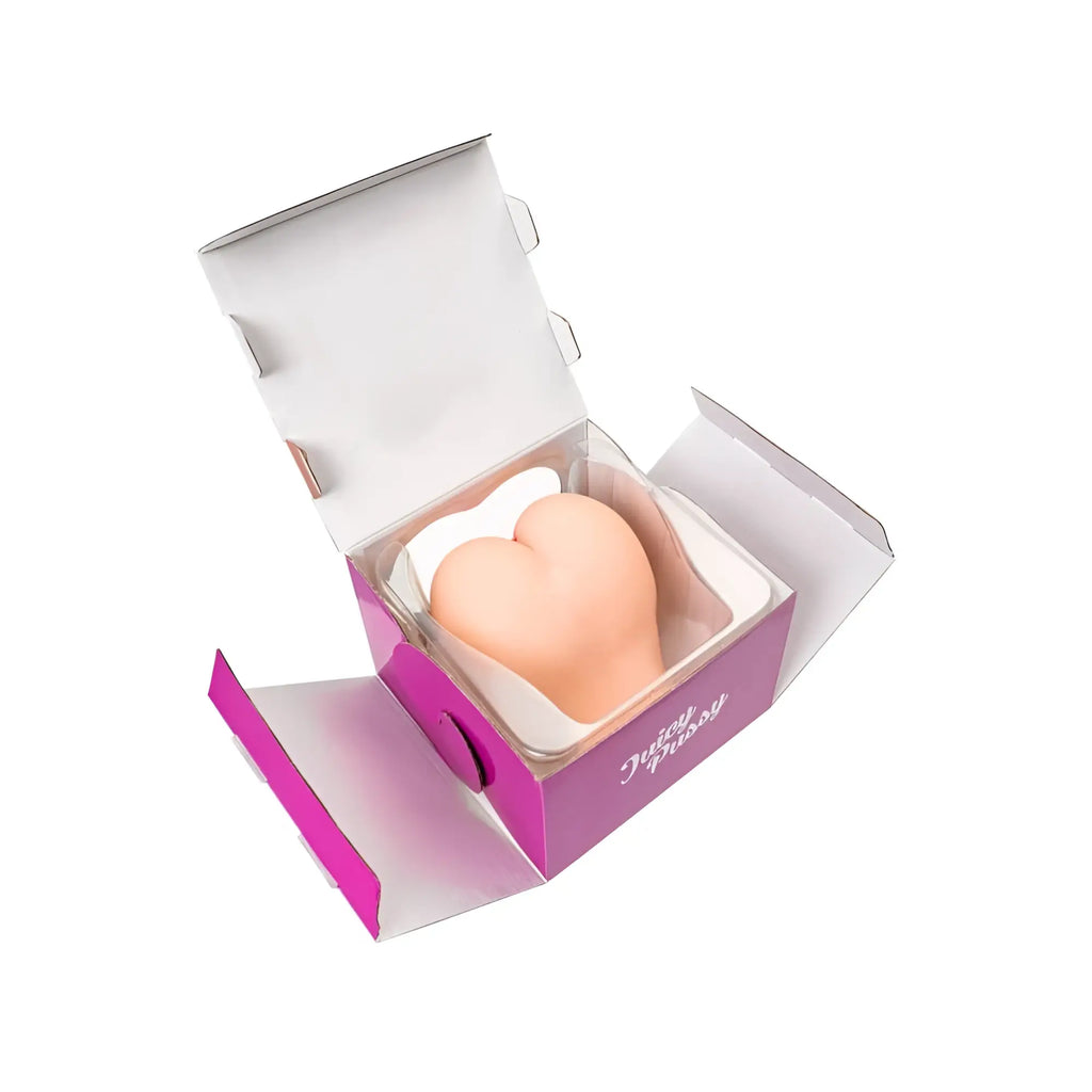 A soft peach-colored heart-shaped silicone eraser in a white cushion inside an open purple and silver juicy juicy butt masturbator paula box