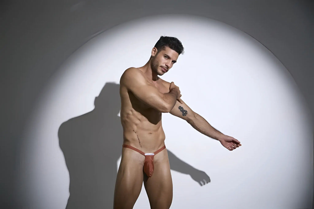 A man wearing a reddish-brown ochre justin simon xsjbu02 bulge thong jockstrap with thin straps and a white label at front