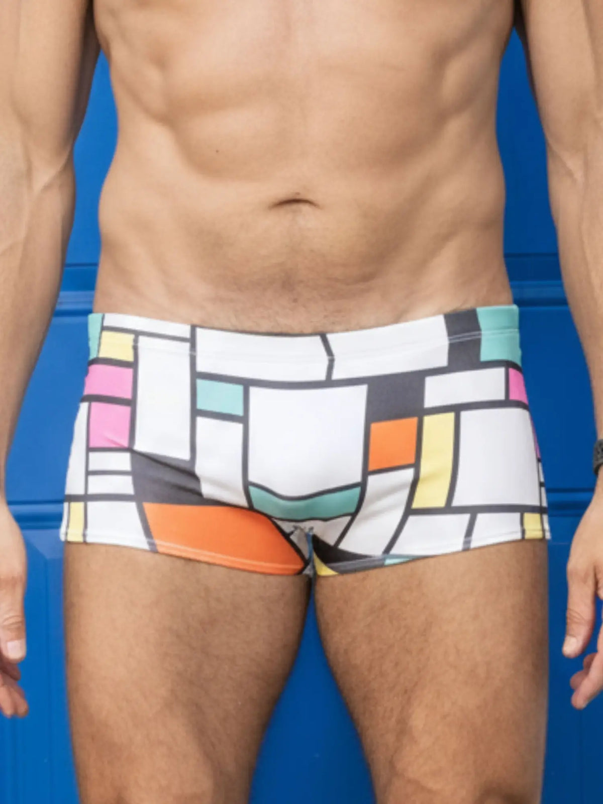 White swim trunks with bold geometric blocks of pink orange yellow teal and black little boy blue design billy suit