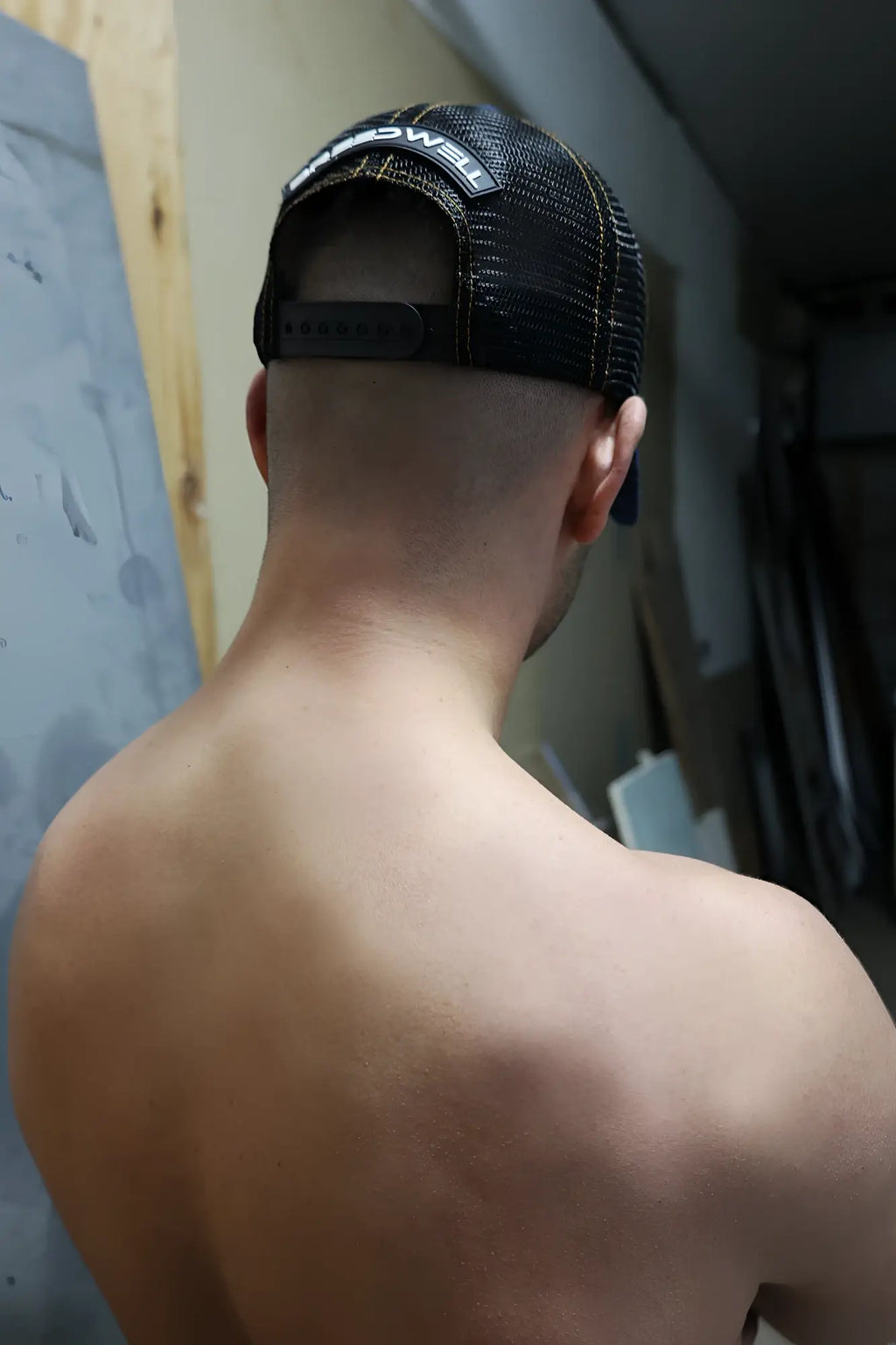 Back view of black loaded denim trucker hat with white embroidered logo and mesh panel for breathability