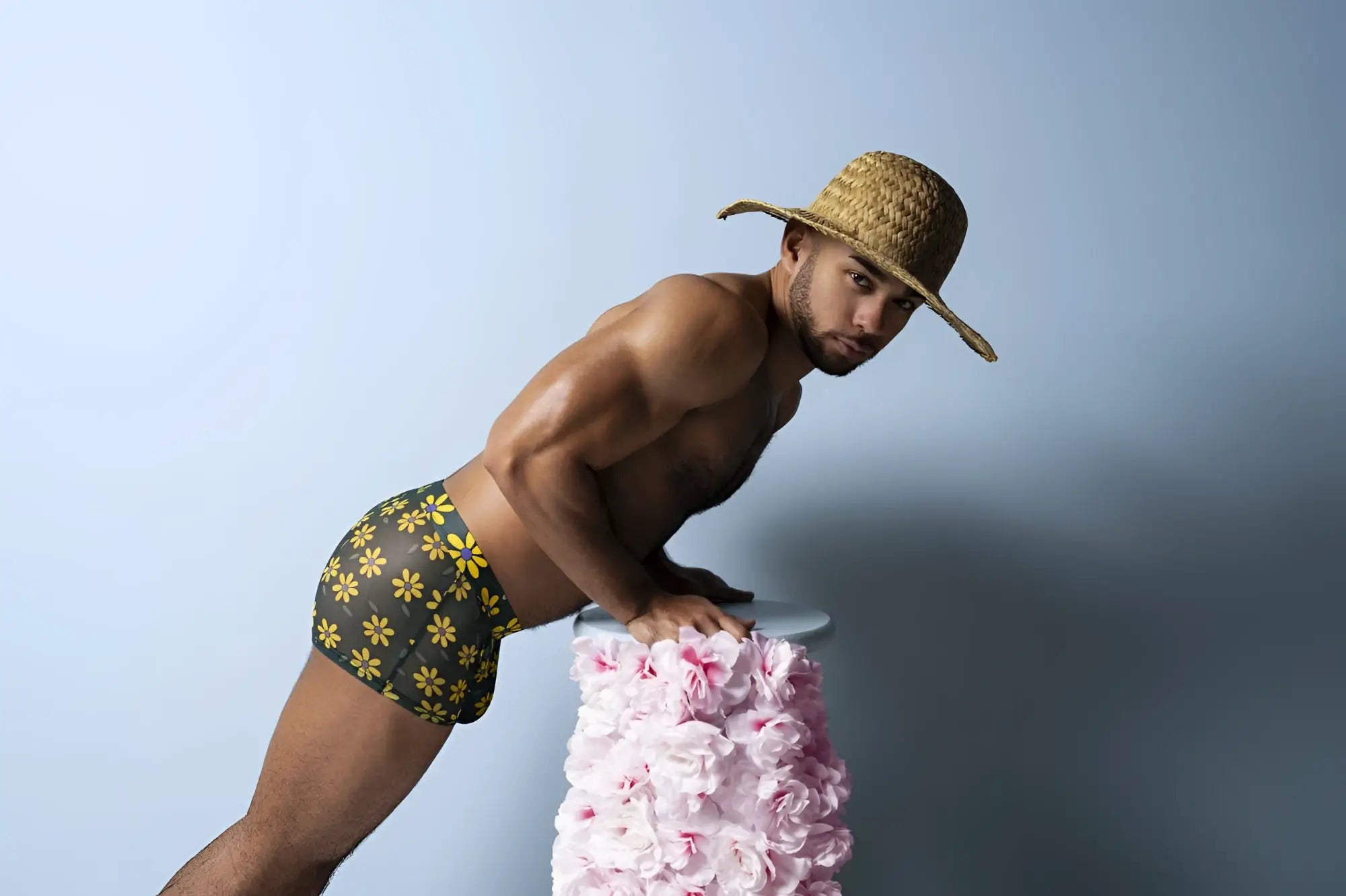 A man wearing male power petal power pouch shorts in black with yellow floral daisy print and a straw hat