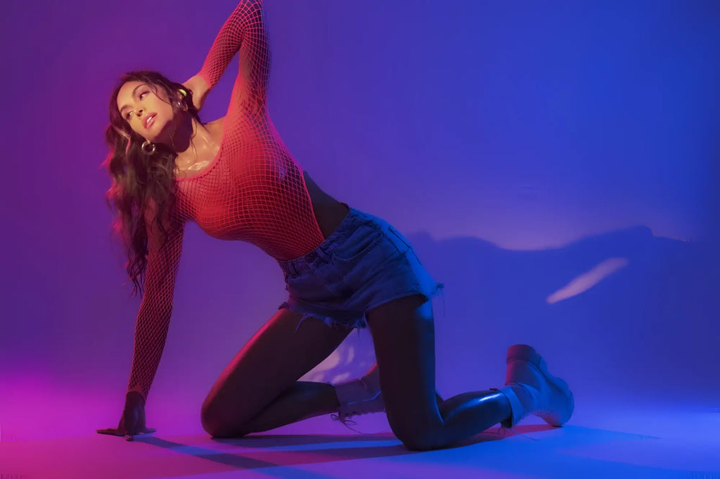 A woman poses dynamically in a neon pink mapale 1119 long sleeve fishnet bodysuit under purple and pink lighting