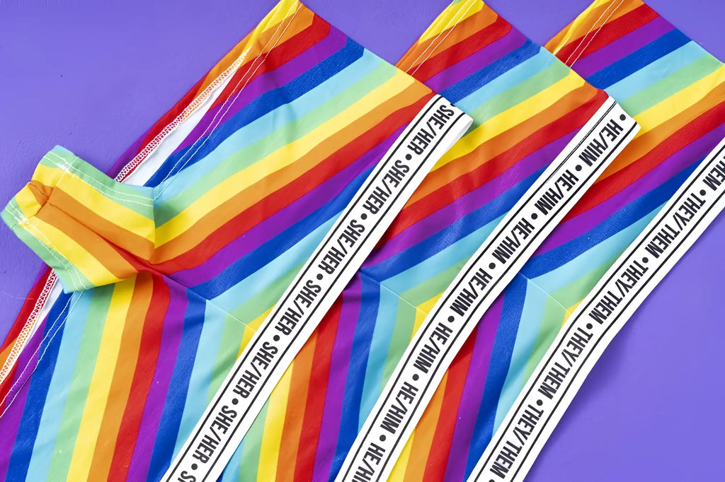 Mapale 122b rainbow cheeky short leggings with rainbow stripes and a white elastic waistband reading she her and they they