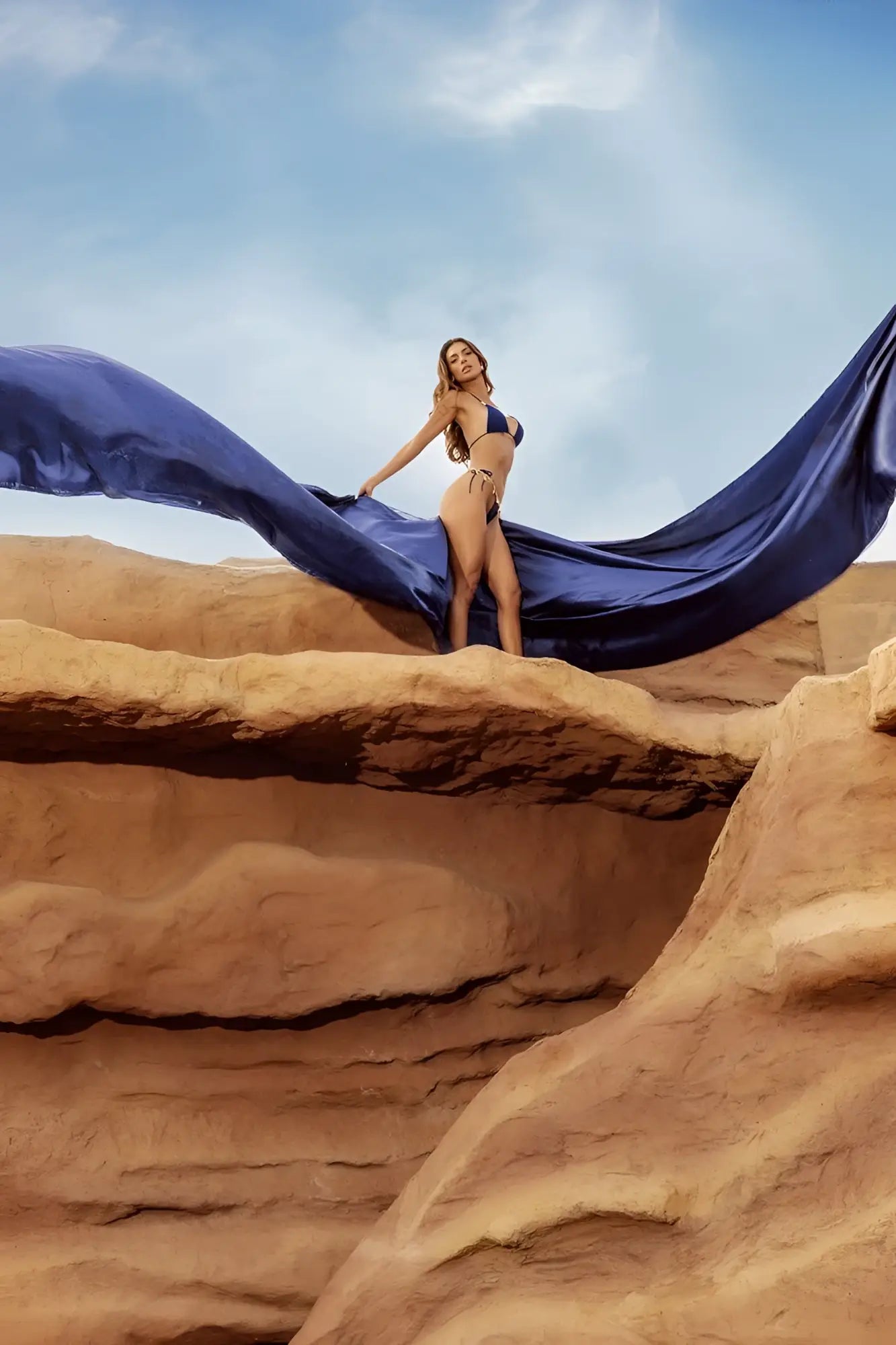 A woman wearing the mapale 67158 deep ocean two piece swimsuit stands on red rocks holding flowing blue fabric