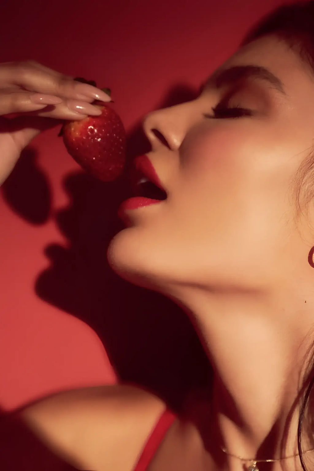 A hand with manicured nails holding a ripe glossy red strawberry beside the mapale 8899 two piece set in black and red
