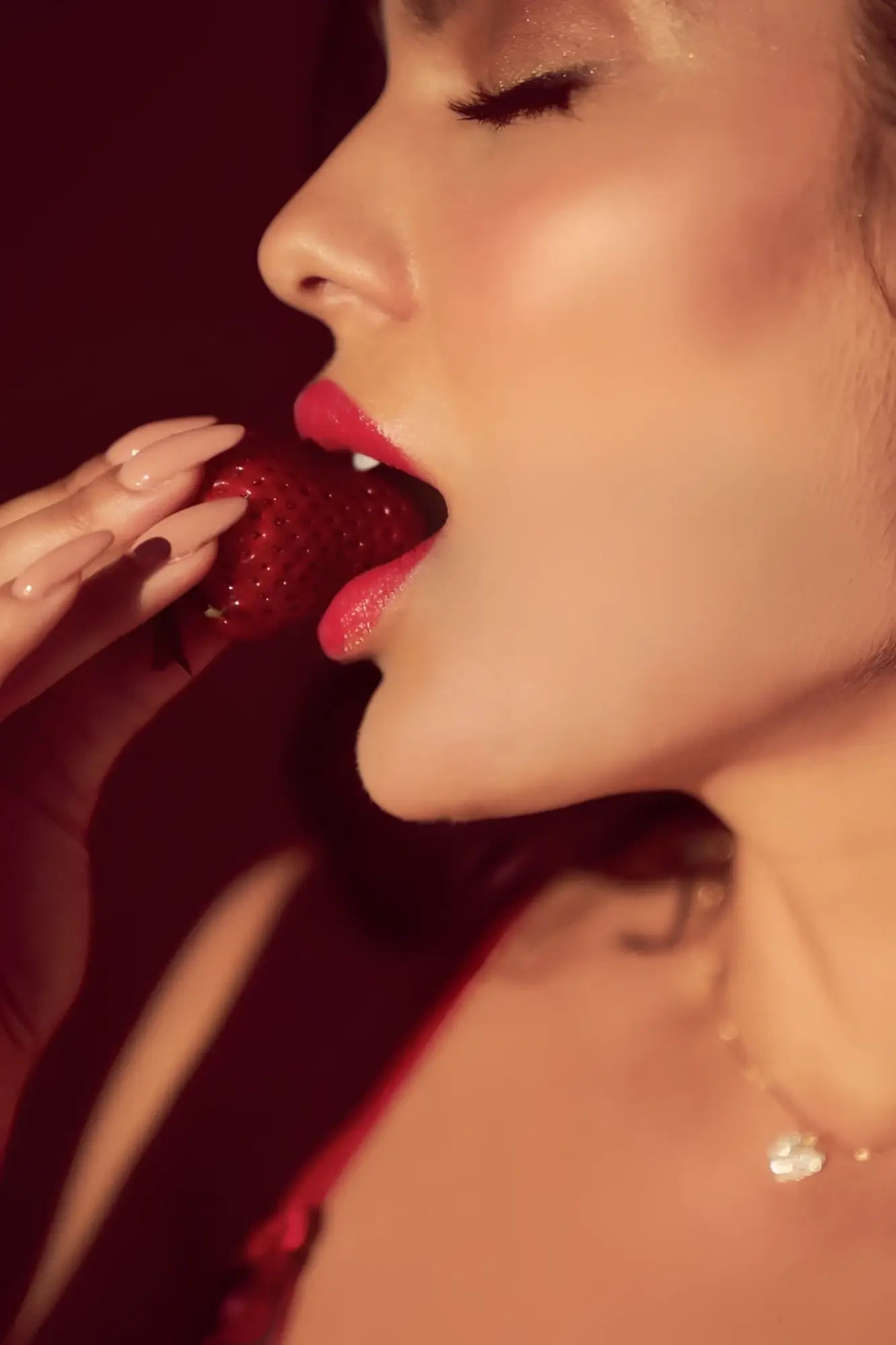 A woman with glossy red lips bites a ripe strawberry wearing a mapale 8899 two piece set in black and red