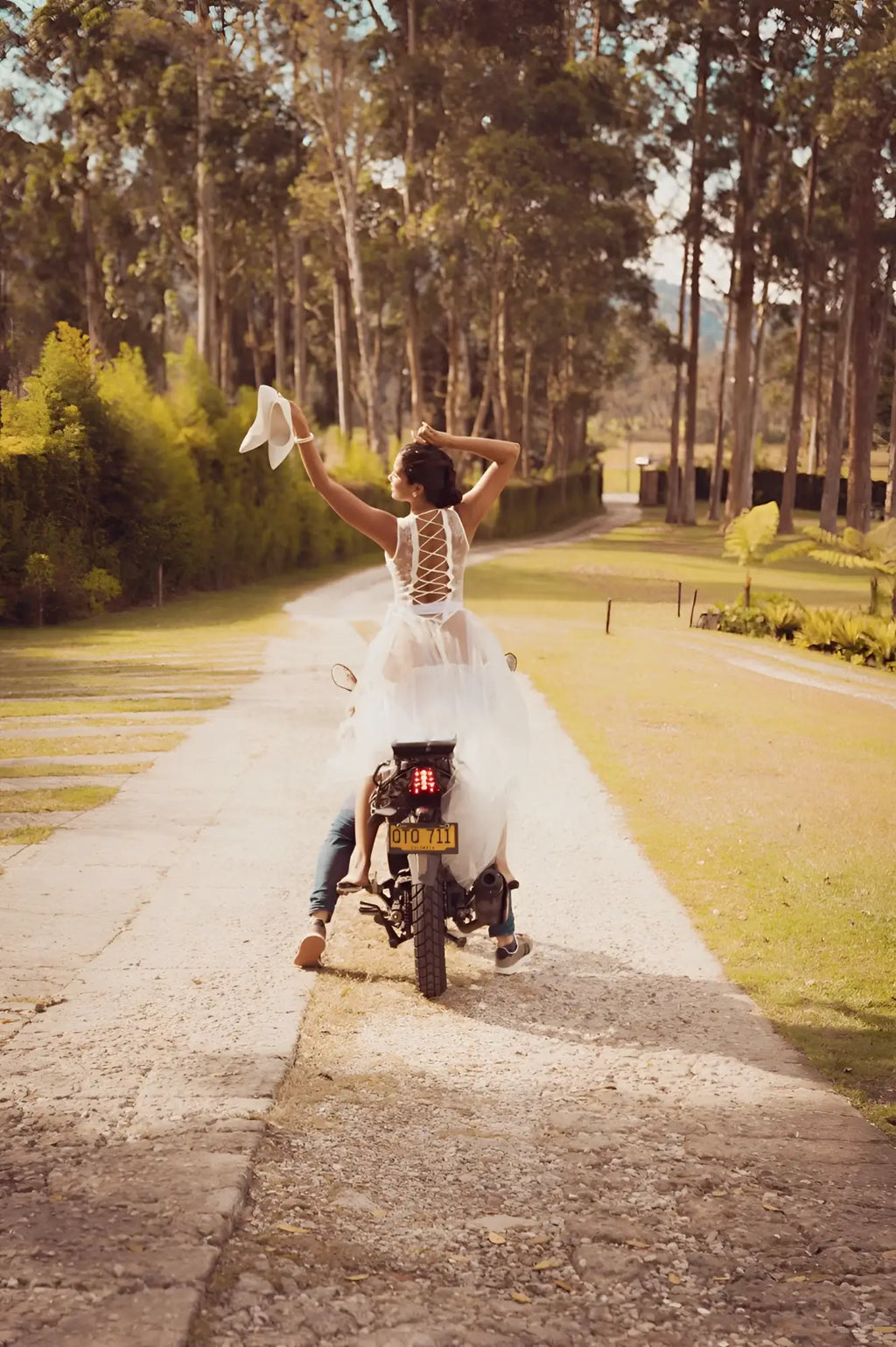 A bride wearing a white lace open back mapale 8932 teddy holding up a veil while riding a motorcycle