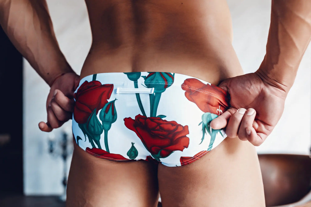 White swim trunks with vibrant red rose and green stem floral pattern from marcuse amour bikini swimwear collection