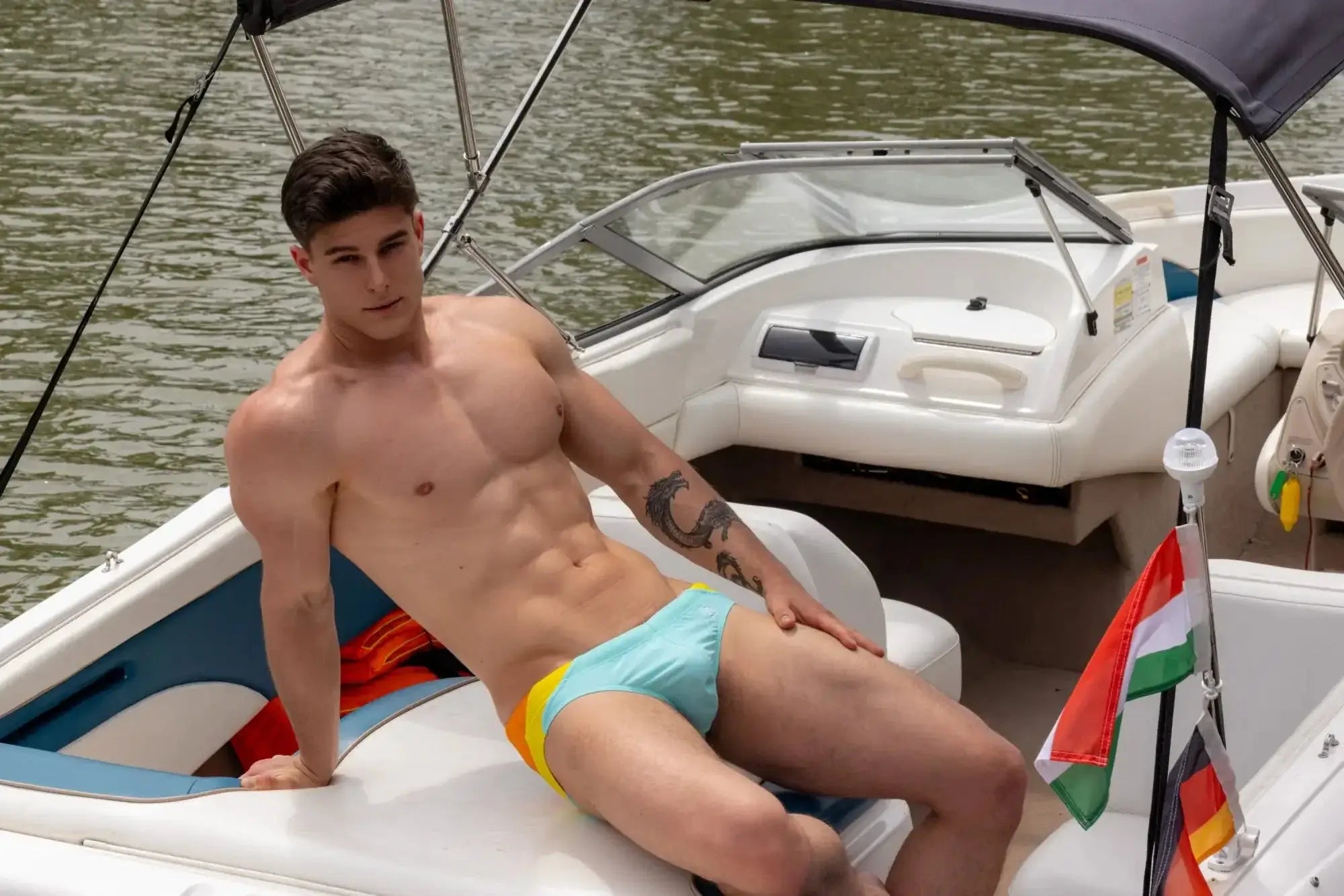 The man is wearing Marcuse Bahama bikini swimwear with bright multicolored swim trunks featuring light blue and yellow panels