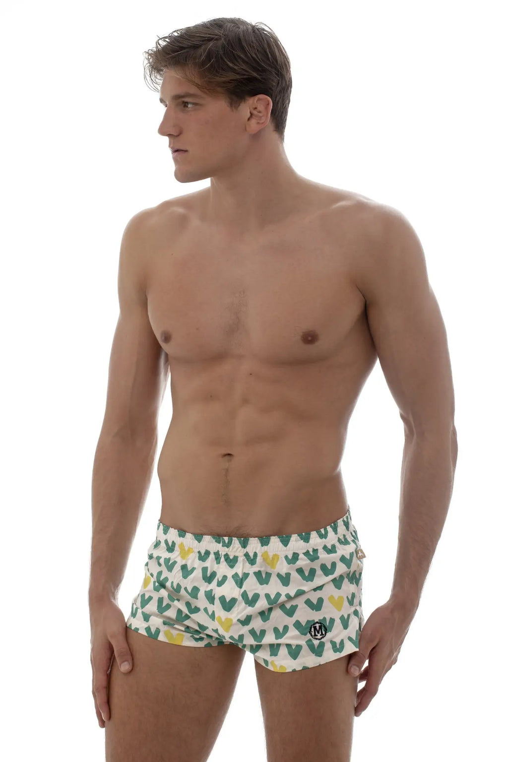 White swim trunks by marcuse featuring a playful green and yellow heart pattern and a small black logo on the right leg