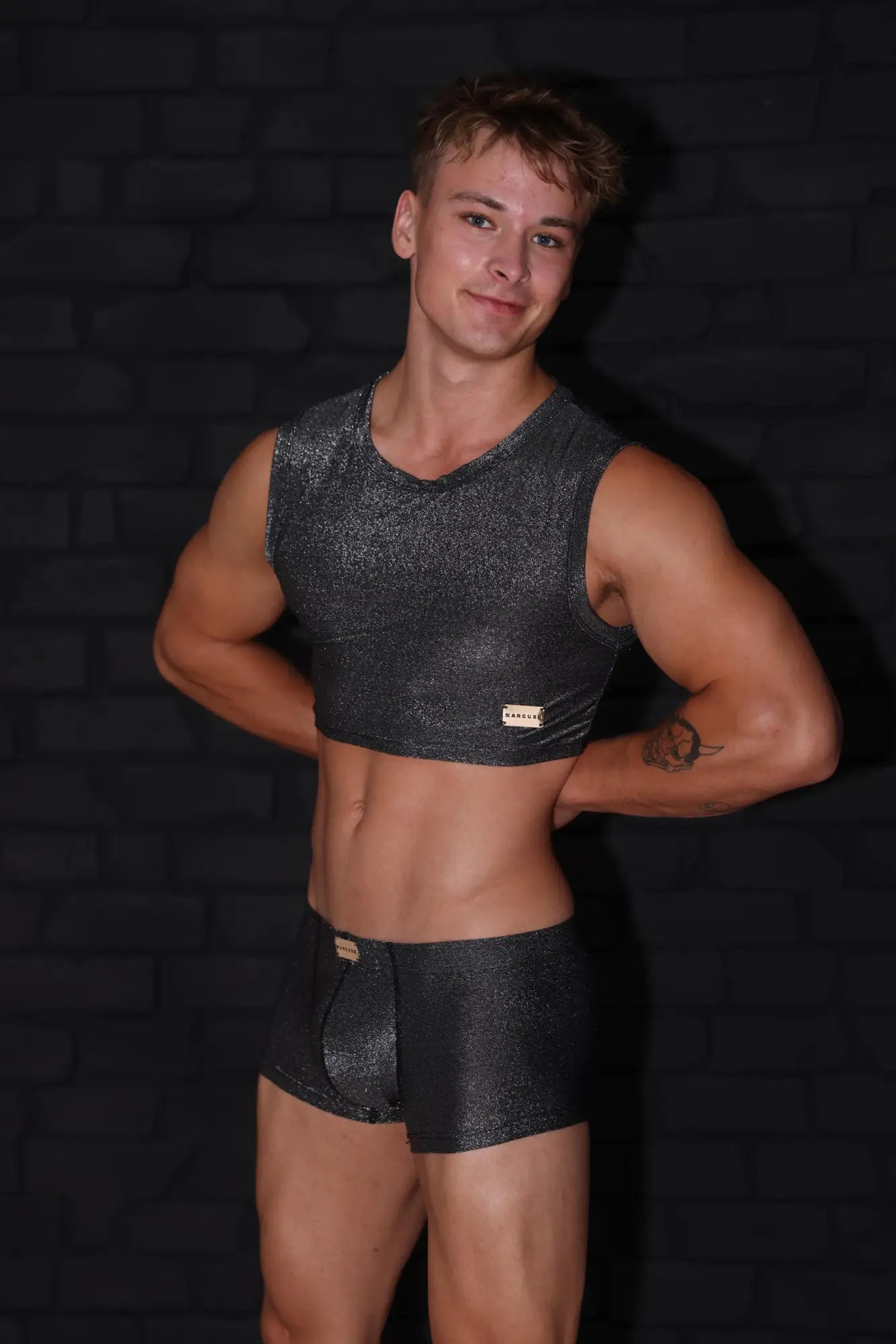 Marcuse glisten top crop tank is a shiny black metallic sleeveless crop top with a small gold logo patch on the front