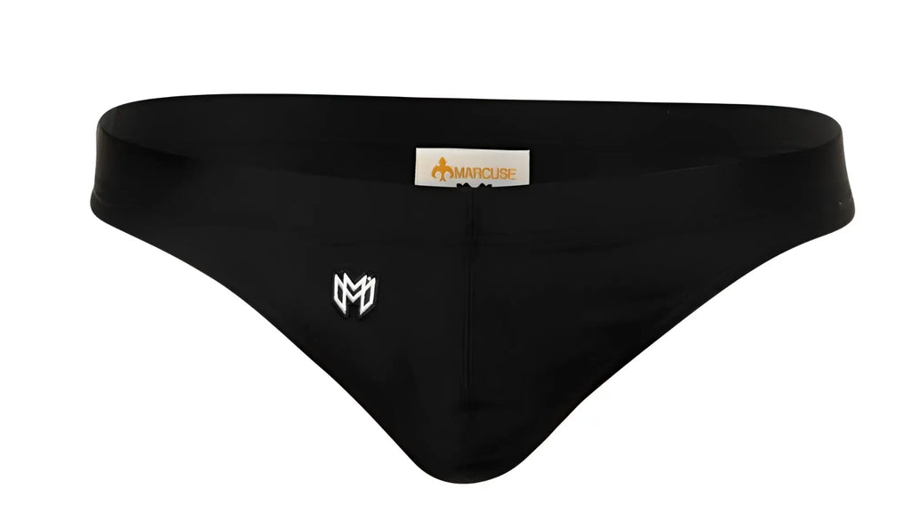 Marcuse Inflate thong swimwear in black swim trunks with white embroidered logo and brand tag visible on front side