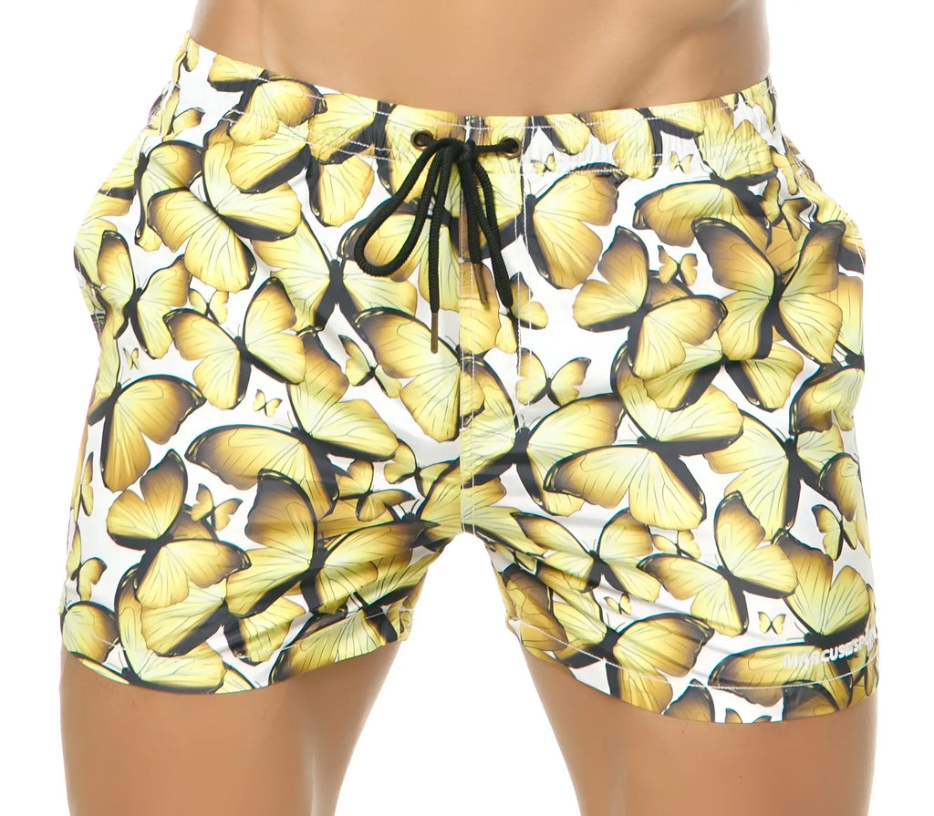 White Marcuse Liberty shorts with vibrant yellow butterfly pattern and black drawstring swim trunks for men
