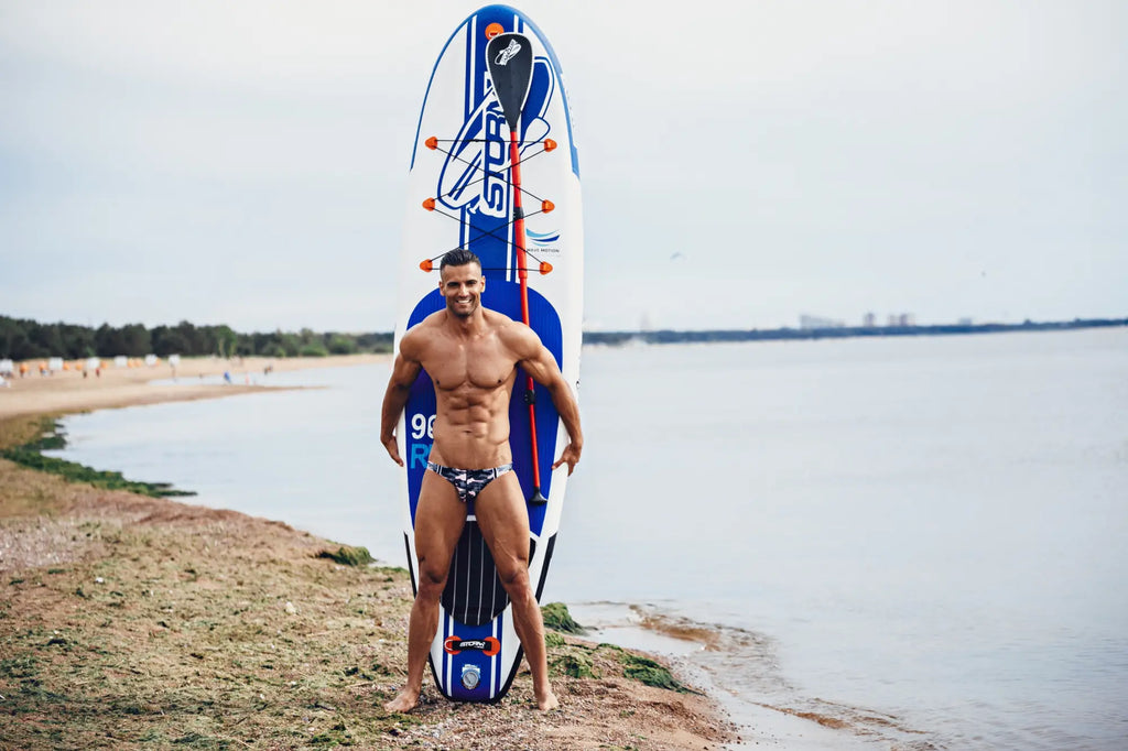 Blue and white inflatable paddleboard with orange accents and black paddle for Marcuse Master Bikini swimwear brand