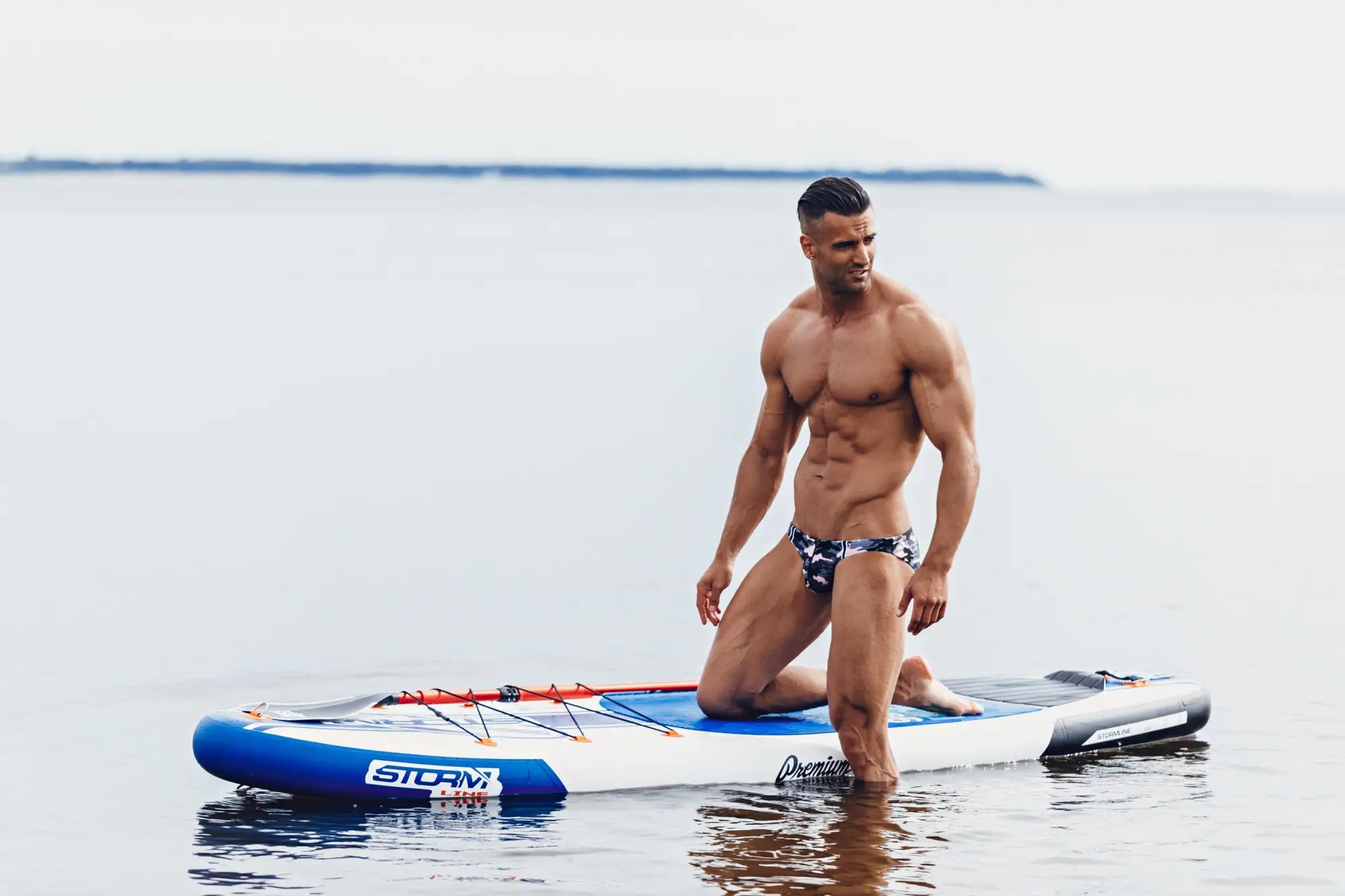 Blue and white inflatable stand-up paddleboard with storm branding shown front side in marcuse master bikini swimwear product image