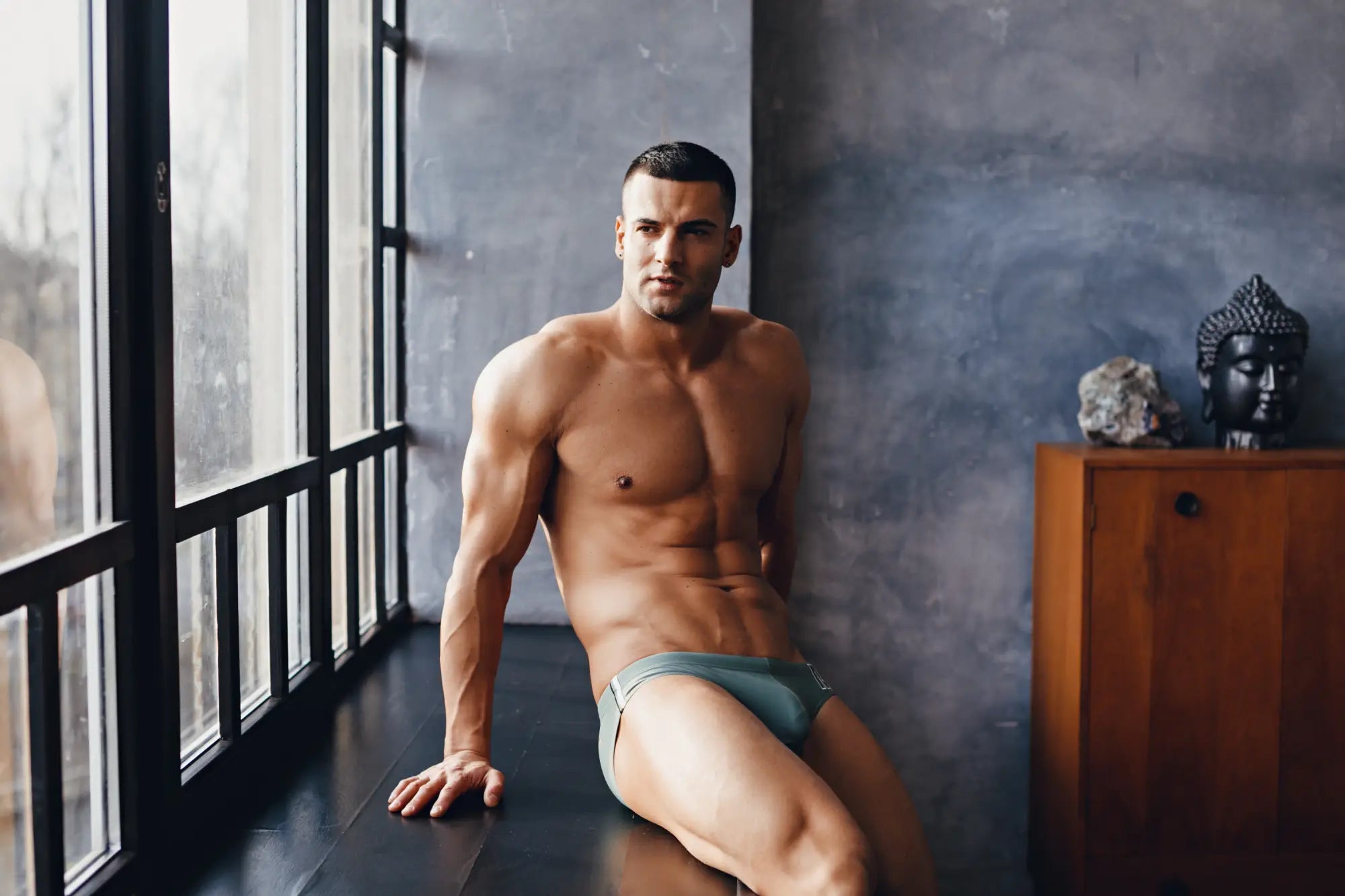 A man wearing light gray form-fitting Marcuse Mpire bikini swimwear briefs showing the front side