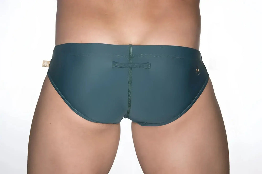 Dark teal marcuse patrol bikini swimwear trunks with central seam and small gold-tone brand tags on each side