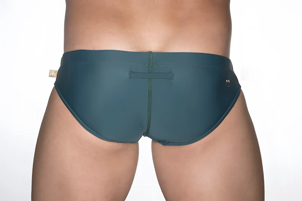 Dark teal marcuse patrol bikini swimwear trunks with central seam and small gold-tone brand tags on each side