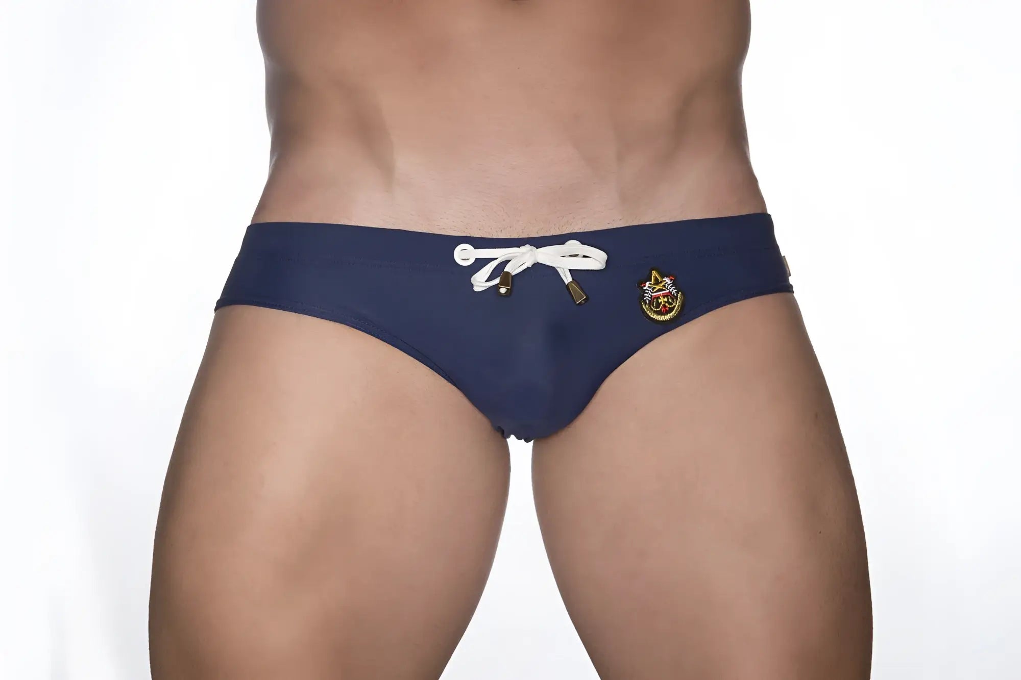 Navy blue Marcuse Patrol bikini swimwear trunks with white drawstring and gold-toned emblem front view