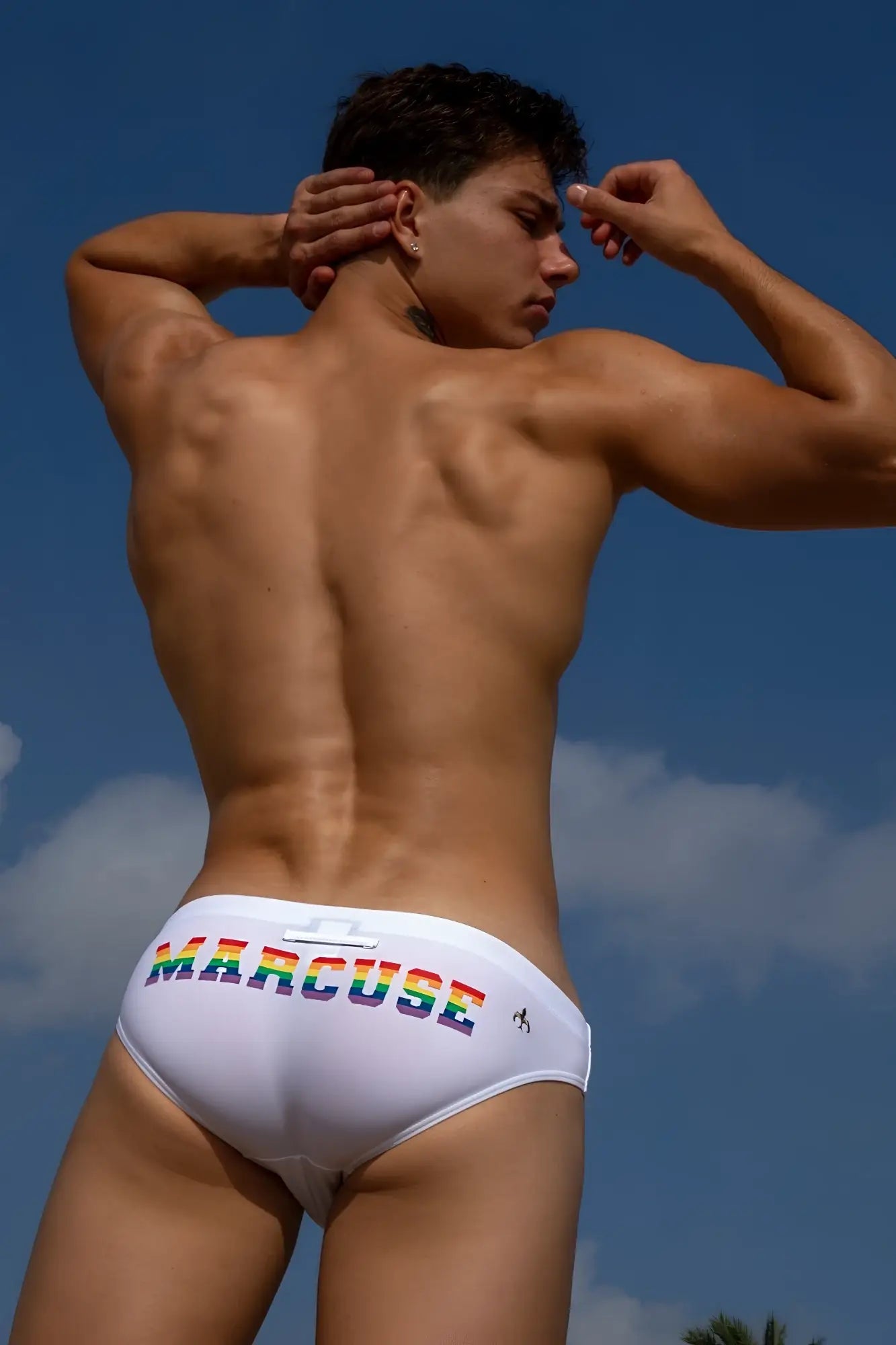 White marcuse swim trunks with rainbow-colored lettering on the waistband from marcuse proud bikini swimwear collection