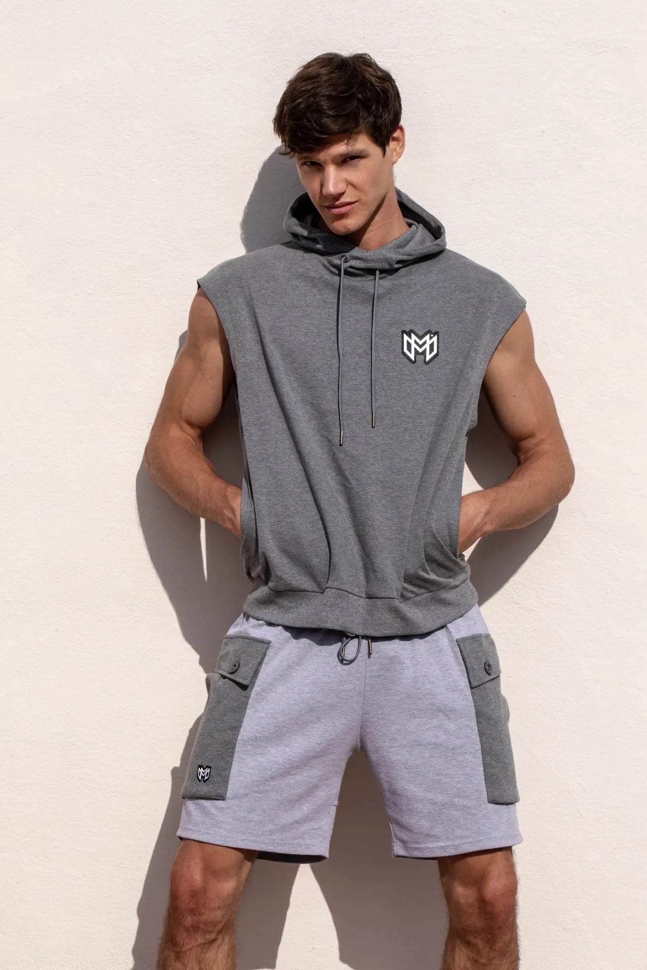 Gray sleeveless hoodie with black and white logo on chest paired with marcuse zaiden cargo shorts
