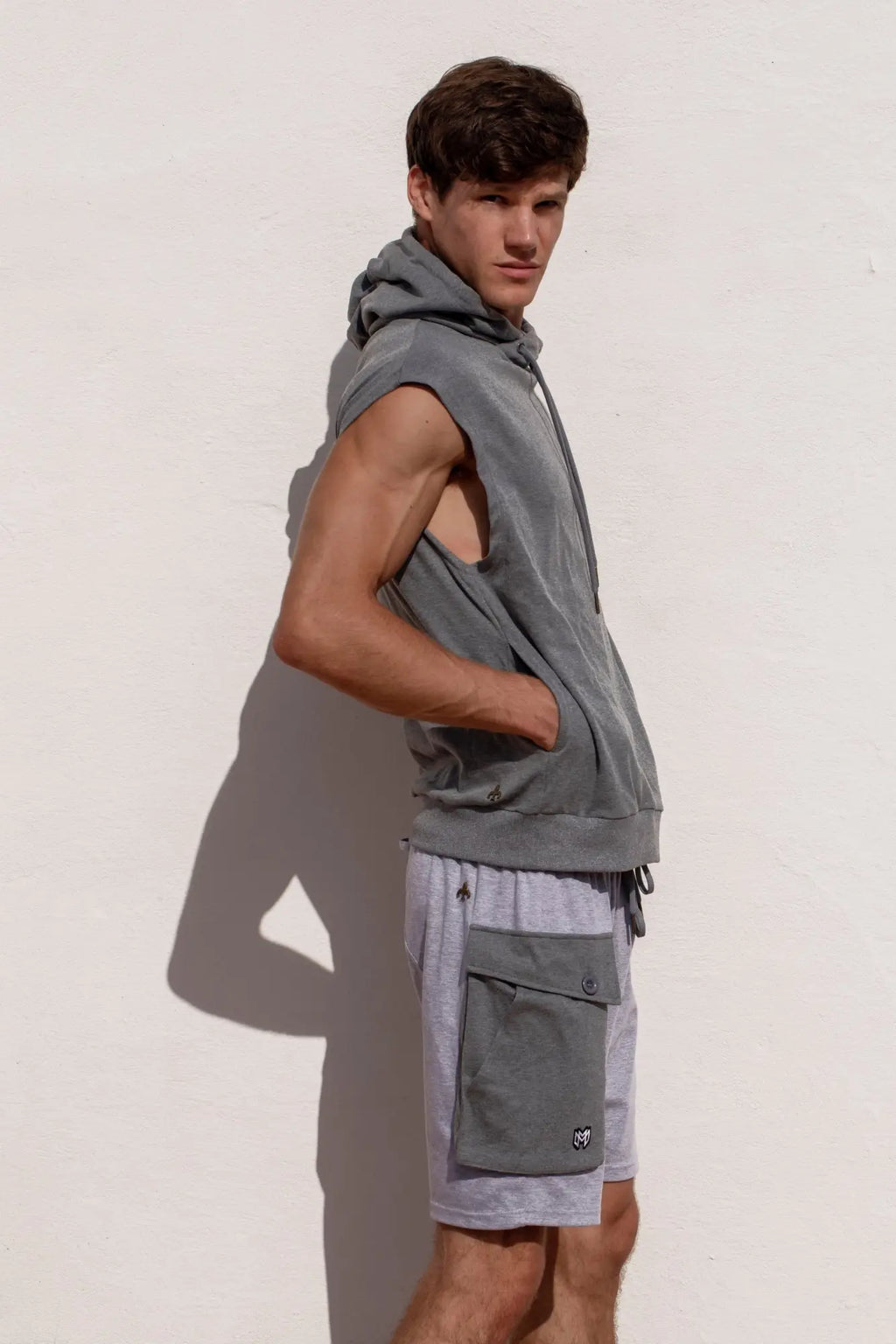 Marcuse Zaiden sleeveless gray hoodie tank top with drawstring hood and front pocket worn over gray cargo shorts