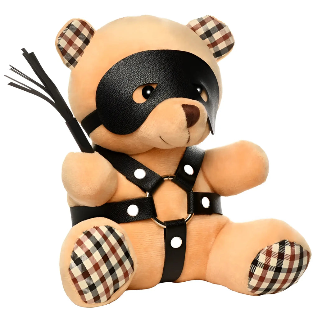 A tan plush teddy bear wearing a black leather mask and harness with plaid patches on ears feet and arms