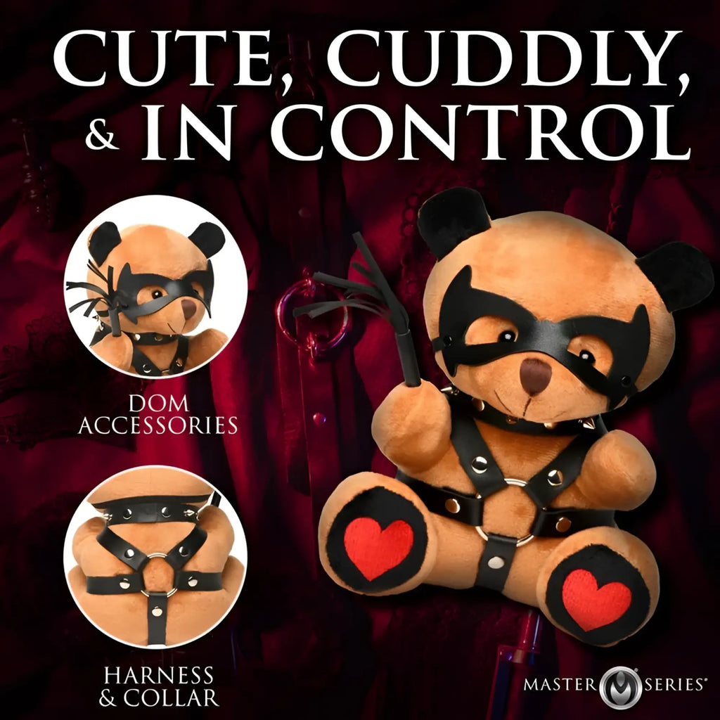 A plush tan teddy bear from master series dom teddy bear plushy wearing a black leather mask harness and collar with red heart patches