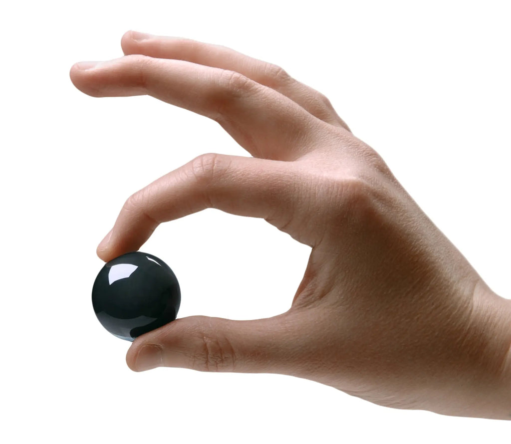 A smooth glossy black jade glass ben wa ball 30mm held delicately between fingers from the master series