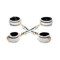 White leather handcuffs with black stripes and gold hardware connected by cross-shaped chain in kink in the dark set