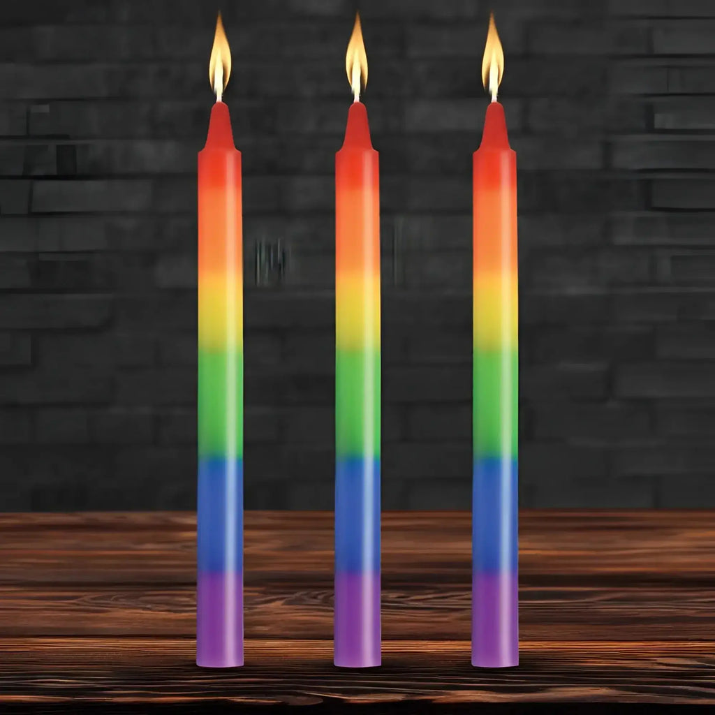 Three slender rainbow-colored taper candles with smooth gradient wax and flickering flames for pride celebration