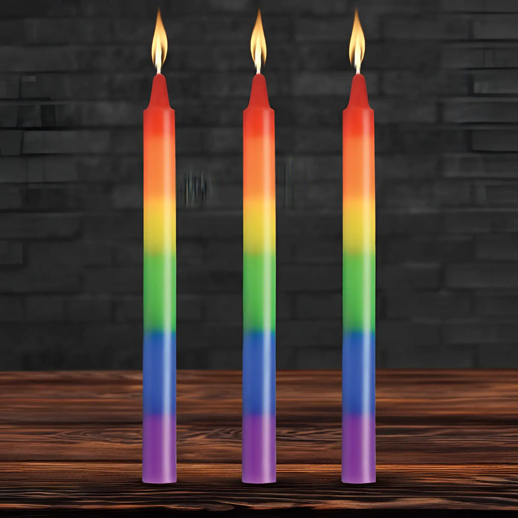 Three slender rainbow-colored taper candles with smooth gradient wax and flickering flames for pride celebration