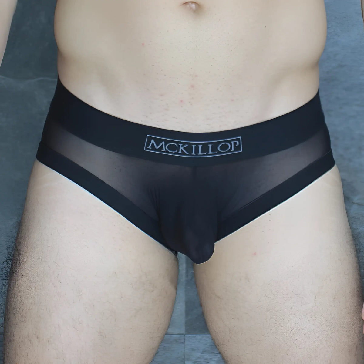 Black sheer mesh briefs with a solid black waistband featuring mckillop branding from the obus hoist brief ultra mesh line