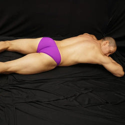 Men's purple bikini underwear by Arroyman featuring a snug fit and smooth fabric shown on a model lying down.