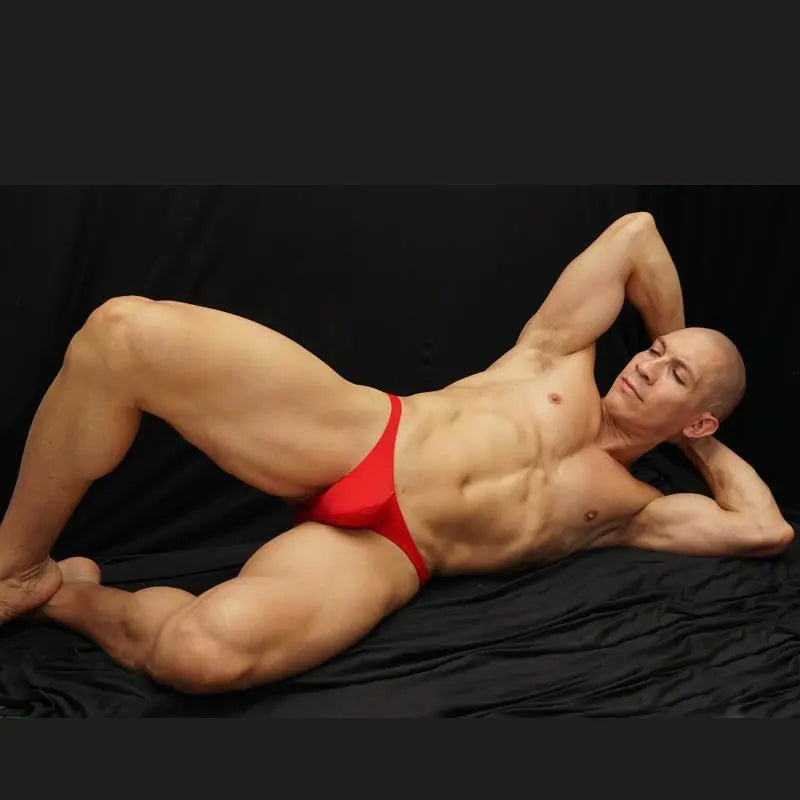Red micro bikini underwear made of soft fabric shown on a model reclining against a black background by Arroyman.