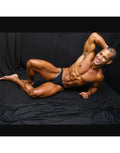 Model wearing black bikini underwear by Arroyman showcasing a smooth fit and minimal coverage against a dark backdrop.