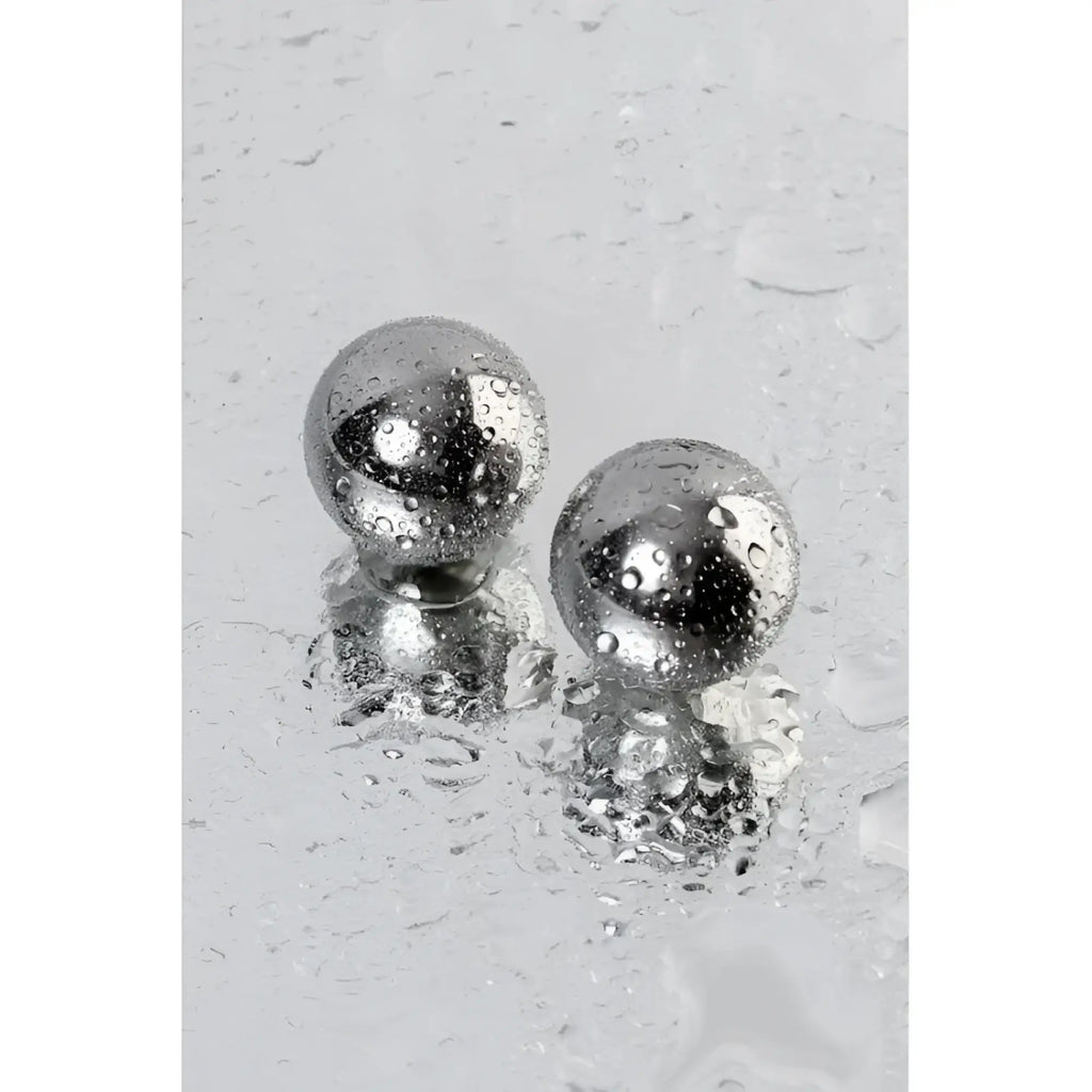 Two polished chrome metal silver vaginal balls 25mm with water droplets reflecting surroundings